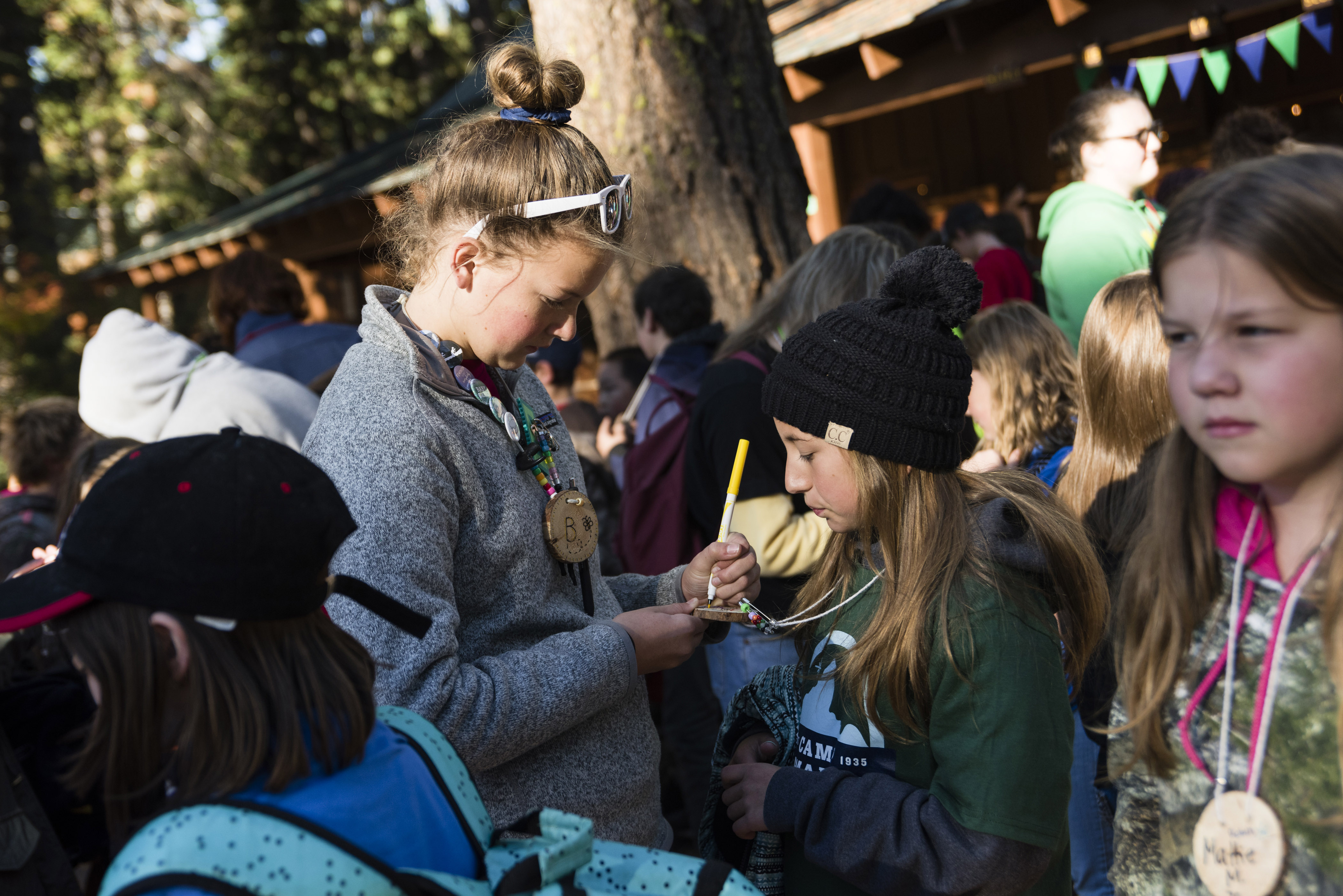 Girl writing on another girl's necklace within a crowd